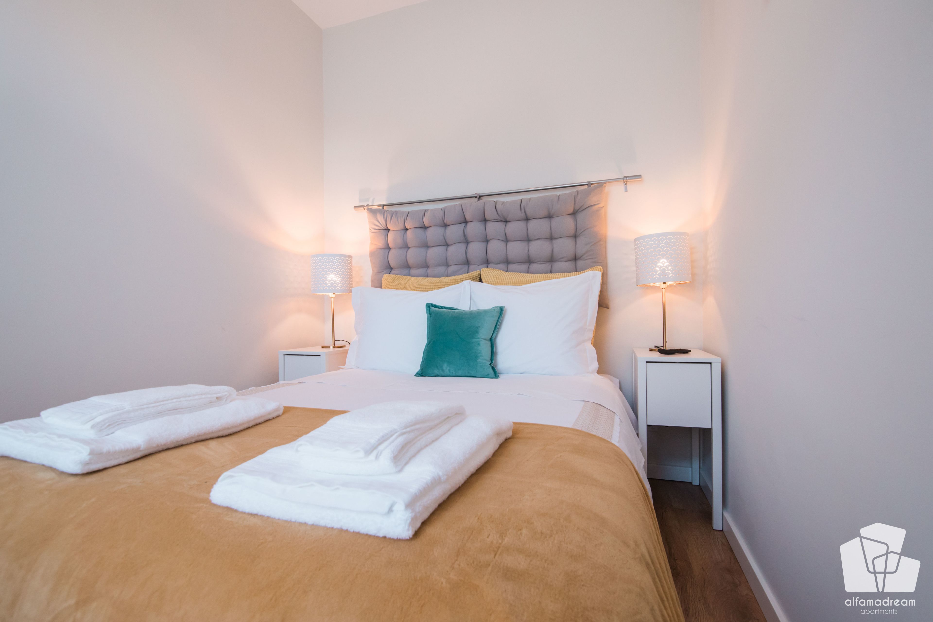 A neatly made bed with two folded towels, a tufted headboard, and two bedside lamps.