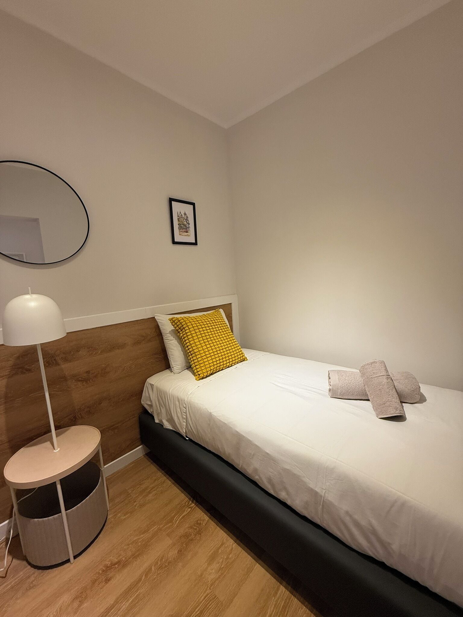 Ein Hotelzimmer mit einem Bett, einem runden Spiegel, einem kleinen Nachttisch und einem Bild an der Wand.