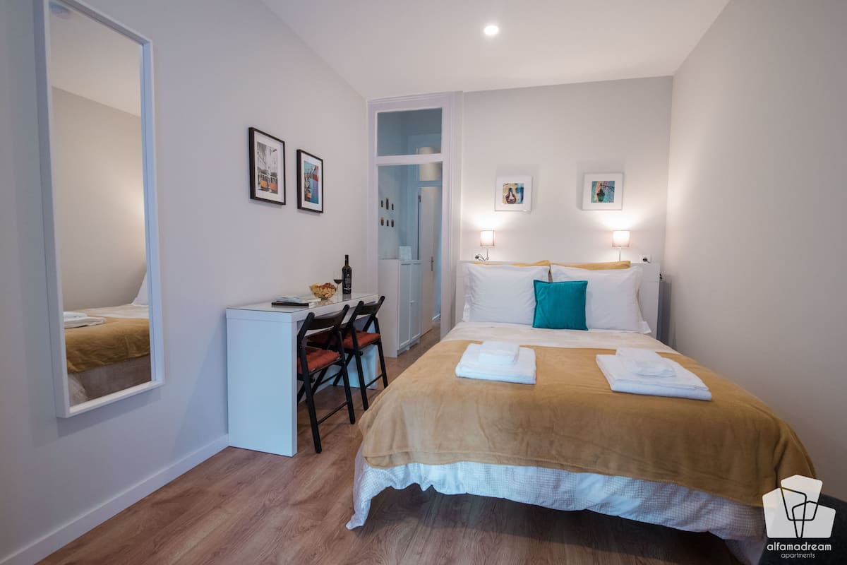 Een slaapkamer met een bed, een bureau en een stoel. Er hangen ingelijste foto's aan de muur.