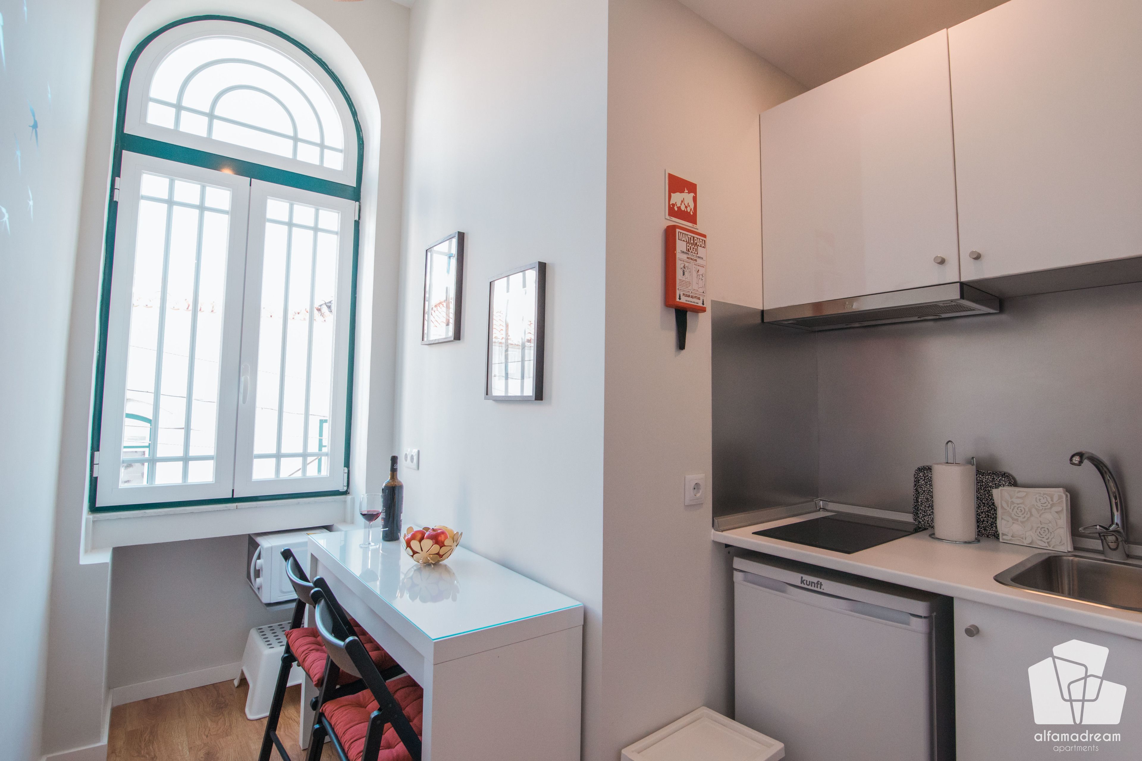 Una cocina compacta con ventana, armarios blancos, un lavamanos y un lavavajillas pequeño.