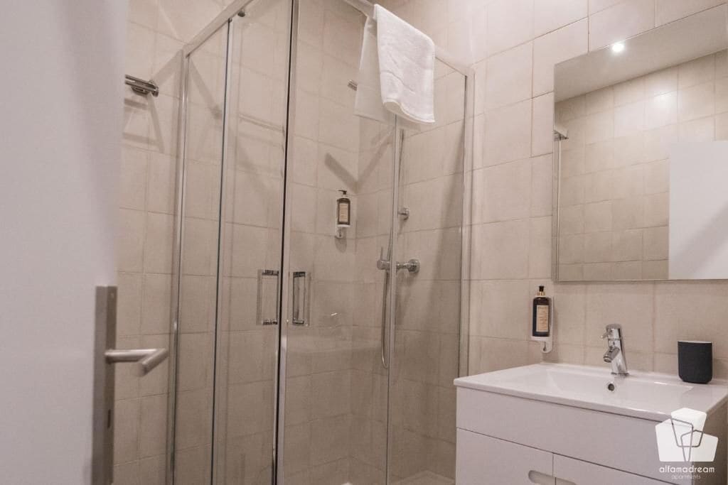 A modern bathroom with a glass-enclosed shower, a white sink, and a mirror above it.