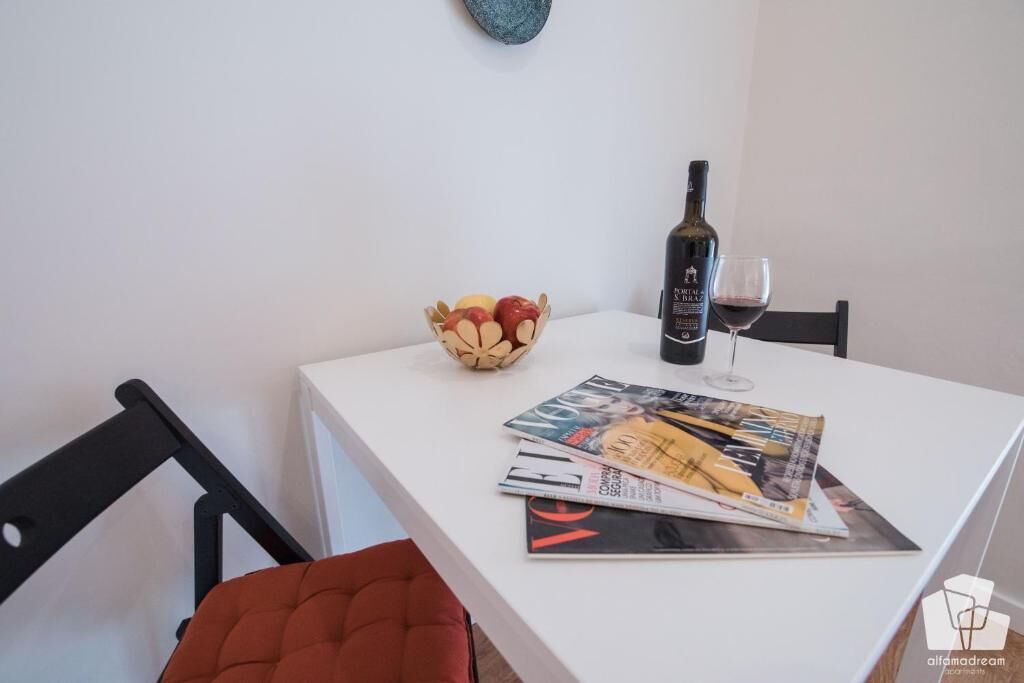 Ett vitt bord med en vinflaska, ett glas och en skål med frukt.
