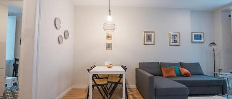 Un salon moderne avec un canapé gris, une petite table blanche sur laquelle se trouve un bol, et un luminaire suspendu.