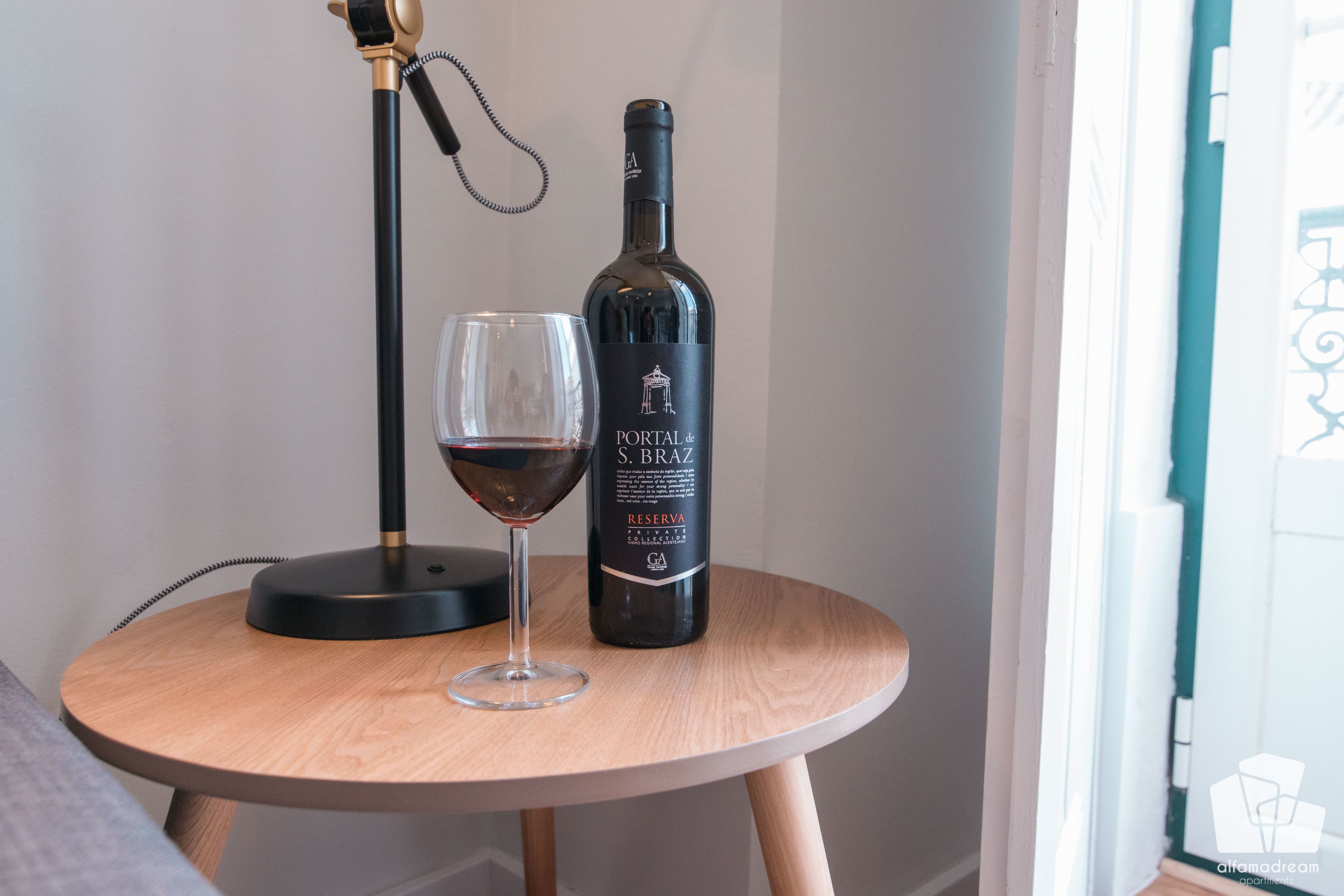 A bottle of wine and a glass on a round wooden table.