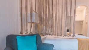 Una habitación con un sillón gris, una cama blanca y una pared con listones de madera verticales.