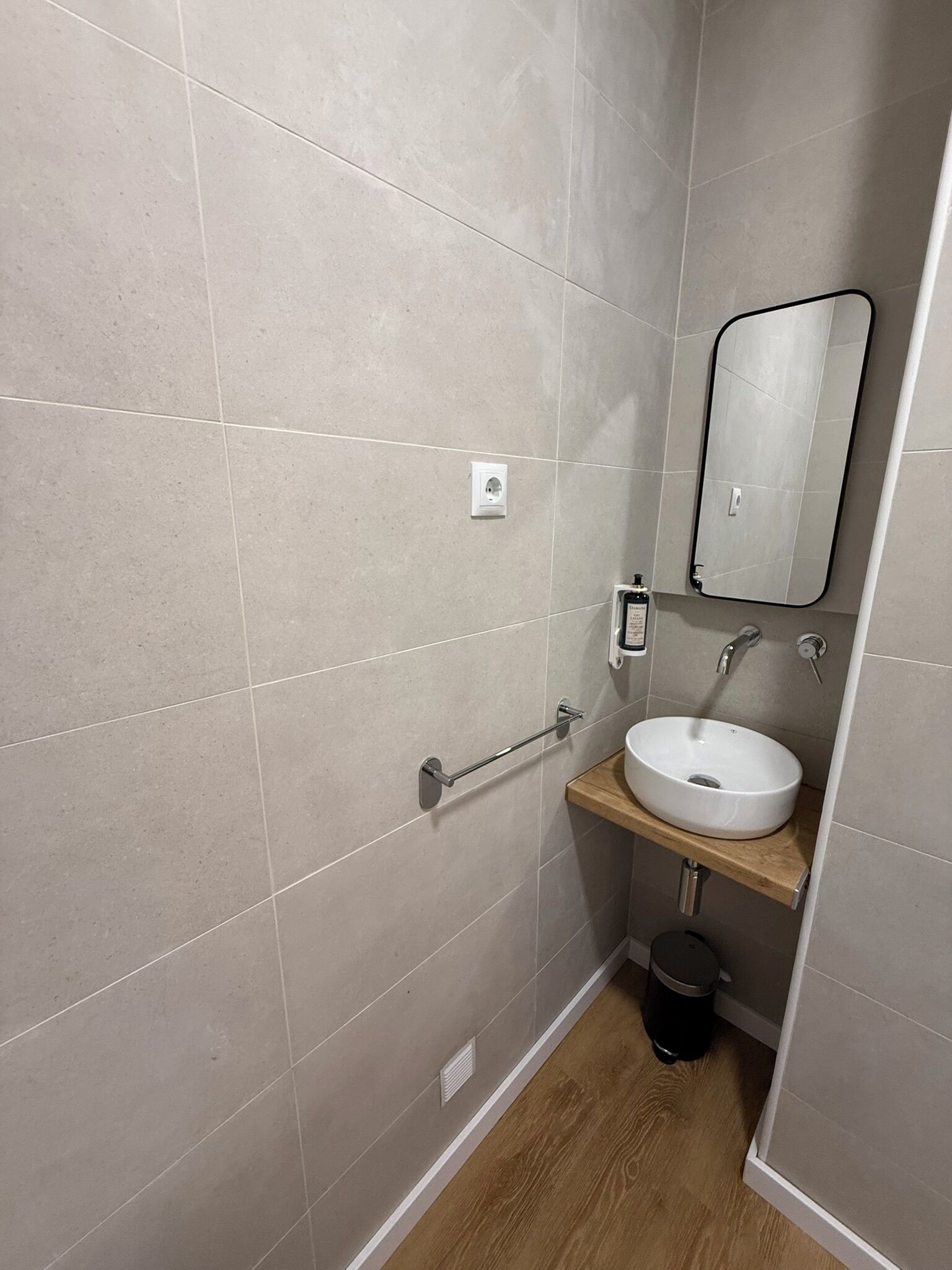 A small bathroom with a white sink, a mirror, and a handrail.