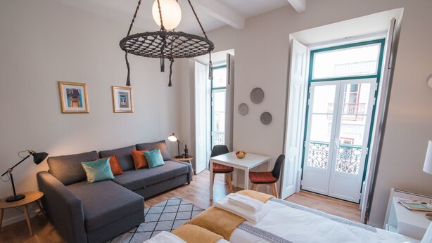 Un dormitorio moderno con cama, sofá, mesa de comedor y una silla. Se ve una ventana con vistas al exterior.