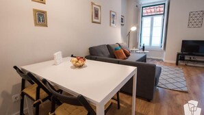 Una sala de estar moderna con una mesa de comedor blanca, un sofá gris y un mueble para televisión.