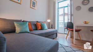 Una sala de estar moderna con un sofá gris, cojines coloridos, una mesita con una lámpara y vistas a través de un ventanal.