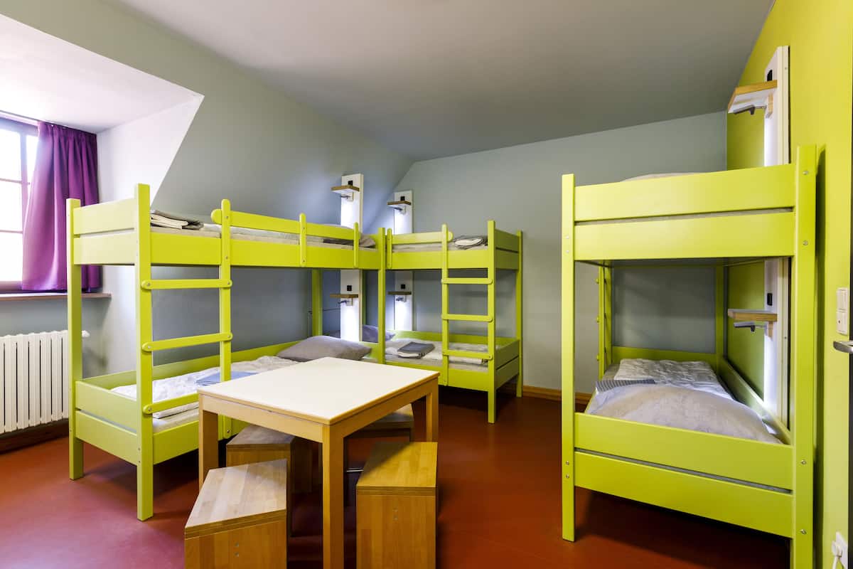 A room with bunk beds, a wooden table, and a window with curtains.