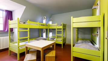 Una habitación con literas, una mesa de madera y un ventanal con cortinas.