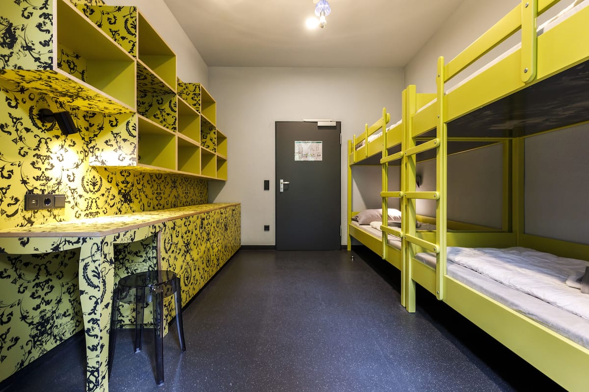 A dormitory room with bunk beds, a desk, and a chair.
