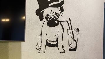 Un mur orné d’une fresque en noir et blanc représentant un chien portant un chapeau haut de forme et tenant un verre à la main.