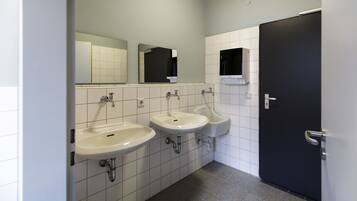 Eine Toilette mit zwei Waschbecken, einem Urinal und einer Tür.