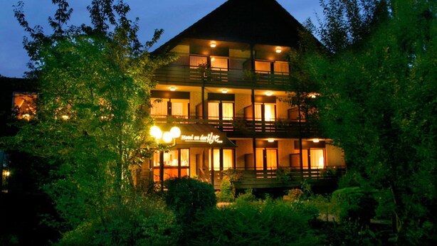 A multi-story hotel with a prominent balcony on the second floor, surrounded by lush greenery. - Hotel an der Ilse (Lemgo)