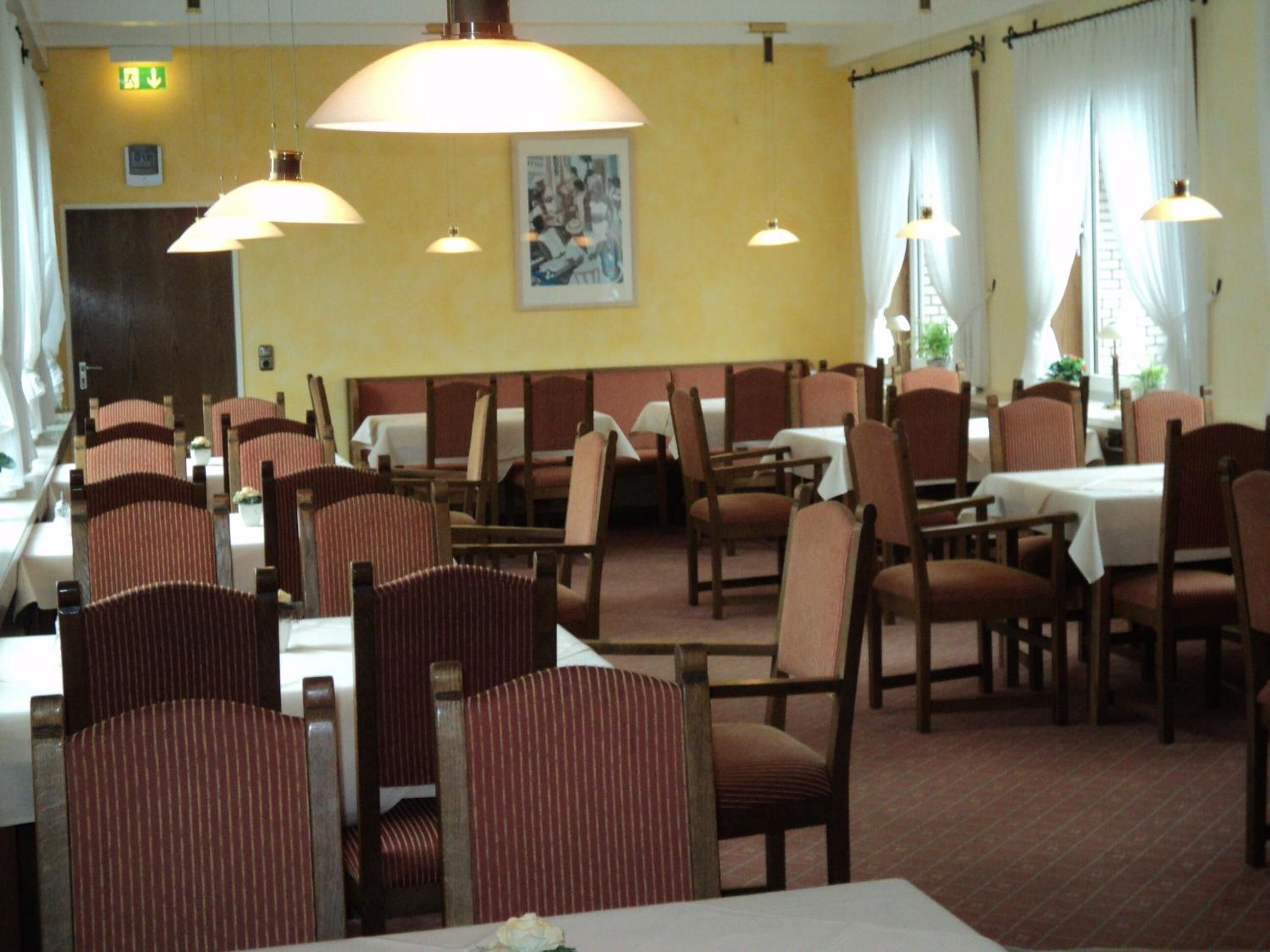 A restaurant with booths and tables, featuring a yellow wall, hanging lamps, and a framed picture.