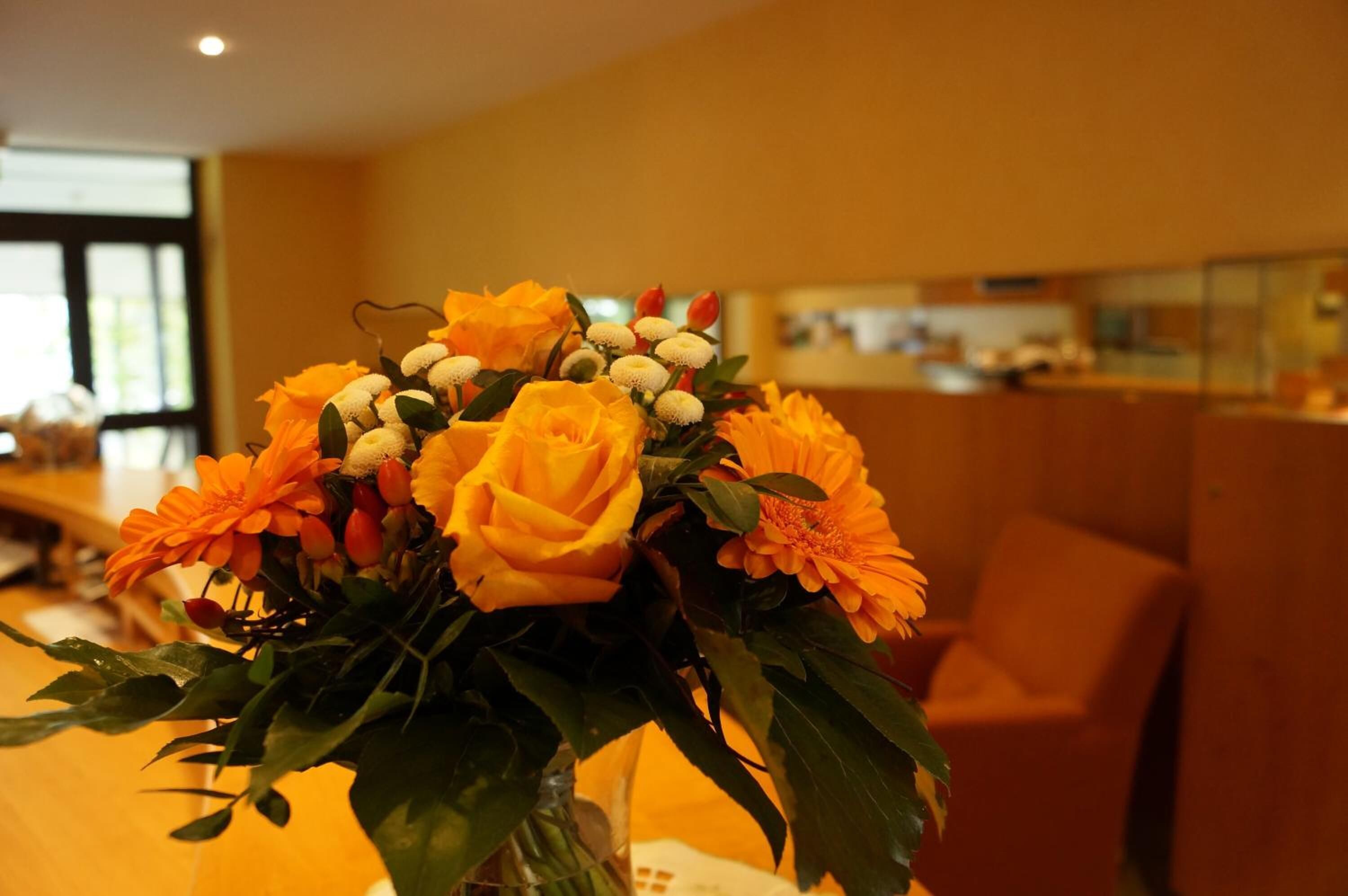 A bouquet of flowers in a vase on a table in a room with a window and a chair.