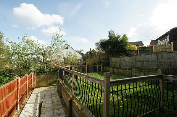 A backyard with a wooden fence, a stone pathway, and a grassy area. - 3 Bedroom Holiday Home With River Views (Frodsham)