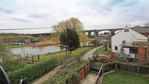 A riverside view with a bridge, a white building with a sloped roof, and a fenced garden area. - 3 Bedroom Holiday Home With River Views (Frodsham)