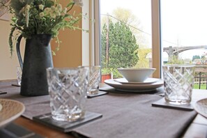 A dining table with a vase of flowers, clear glassware, and plates, set against a window with a view of a bridge and greenery. - 3 Bedroom Holiday Home With River Views (Frodsham)