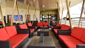 A lounge area with red and black wicker sofas, a glass coffee table, and a bar area in the background. - Qualibest Grand Hotels (Abuja)