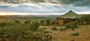 A single-story building with a conical roof, surrounded by sparse vegetation and hills in the background. - Elewana Loisaba Lodo Springs (Loisaba)