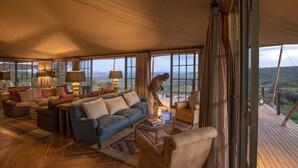 A spacious living area with a large sofa, armchairs, and a coffee table. There are multiple lamps and a view of the outdoors through large windows. - Elewana Loisaba Lodo Springs (Loisaba)