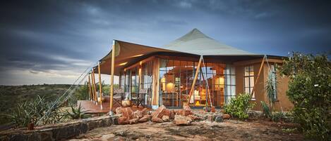 A modern, spacious lodge with a large glass facade, a stone-paved entrance, and a surrounding natural landscape.