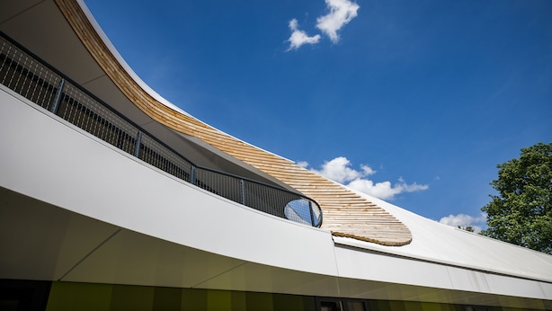 Un edificio moderno con fachada blanca curva, techo inclinado de madera y una ventana circular.