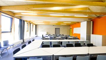 A conference room with tables and chairs, wooden beams on the ceiling, and large windows.