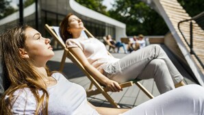 Dos personas descansando en sillones de exterior con un moderno edificio de fondo.