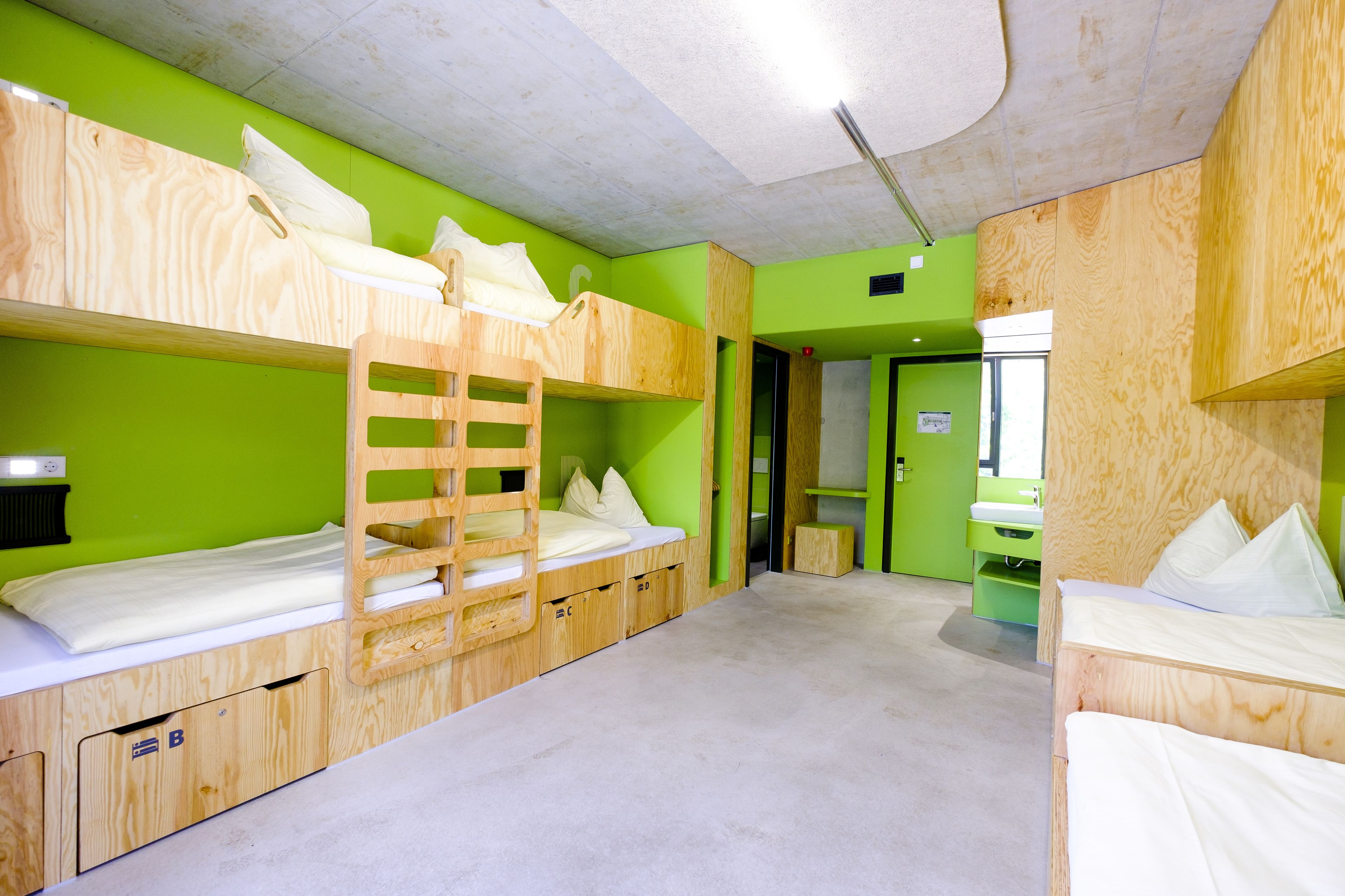 Quarto com beliche, paredes verdes, mobiliário de madeira e um pequeno banheiro.