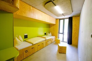 Een knus kamertje met twee bedden, een tafeltje en een raam met gordijnen.