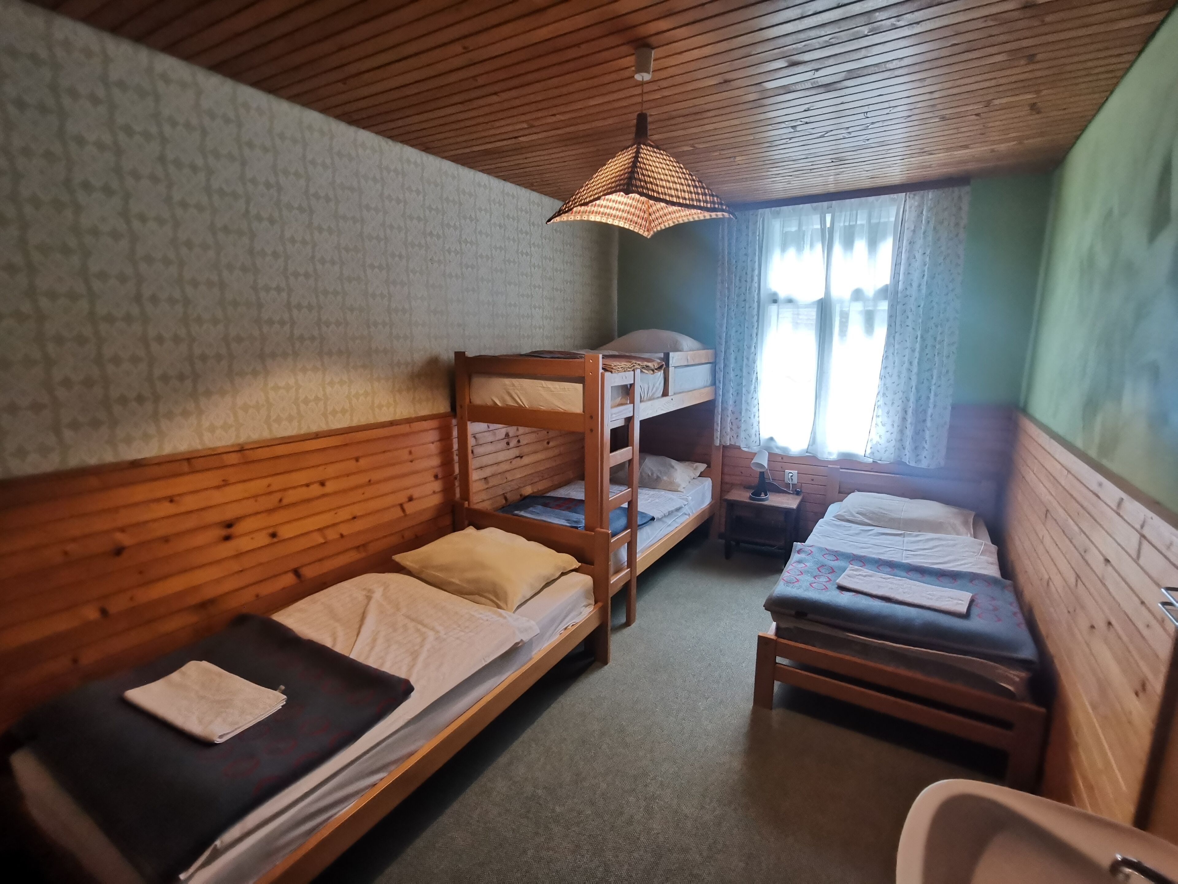 A room with bunk beds, a small table with a lamp, and a window with curtains.