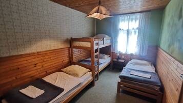 A room with bunk beds, a small table with a lamp, and a window with curtains.