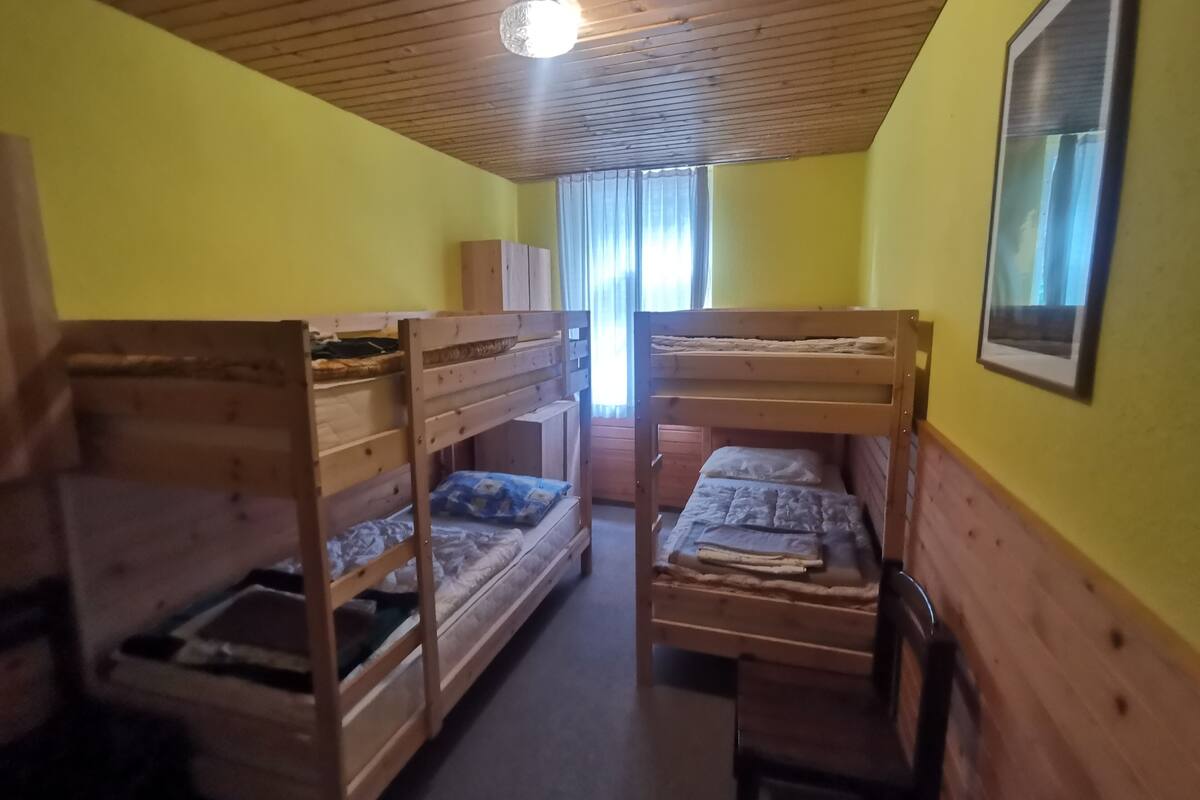 A room with three bunk beds, wooden walls, a ceiling light, and a window with curtains.