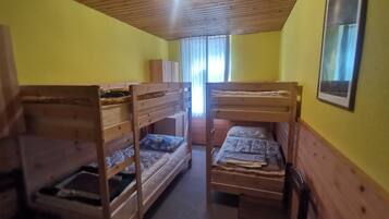 A room with three bunk beds, wooden walls, a ceiling light, and a window with curtains.