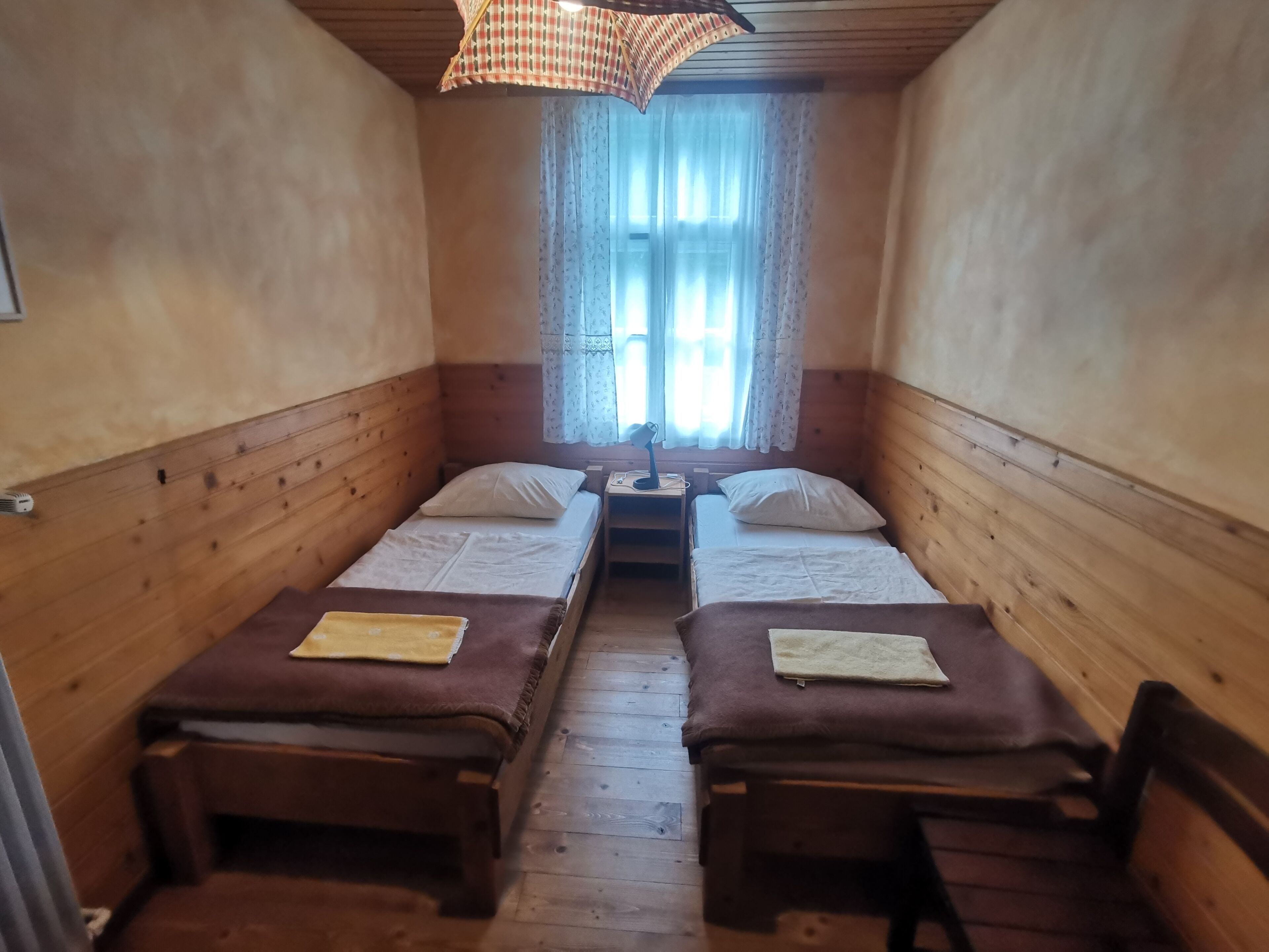 A small, cozy room with two wooden beds, a desk, and a window with curtains.