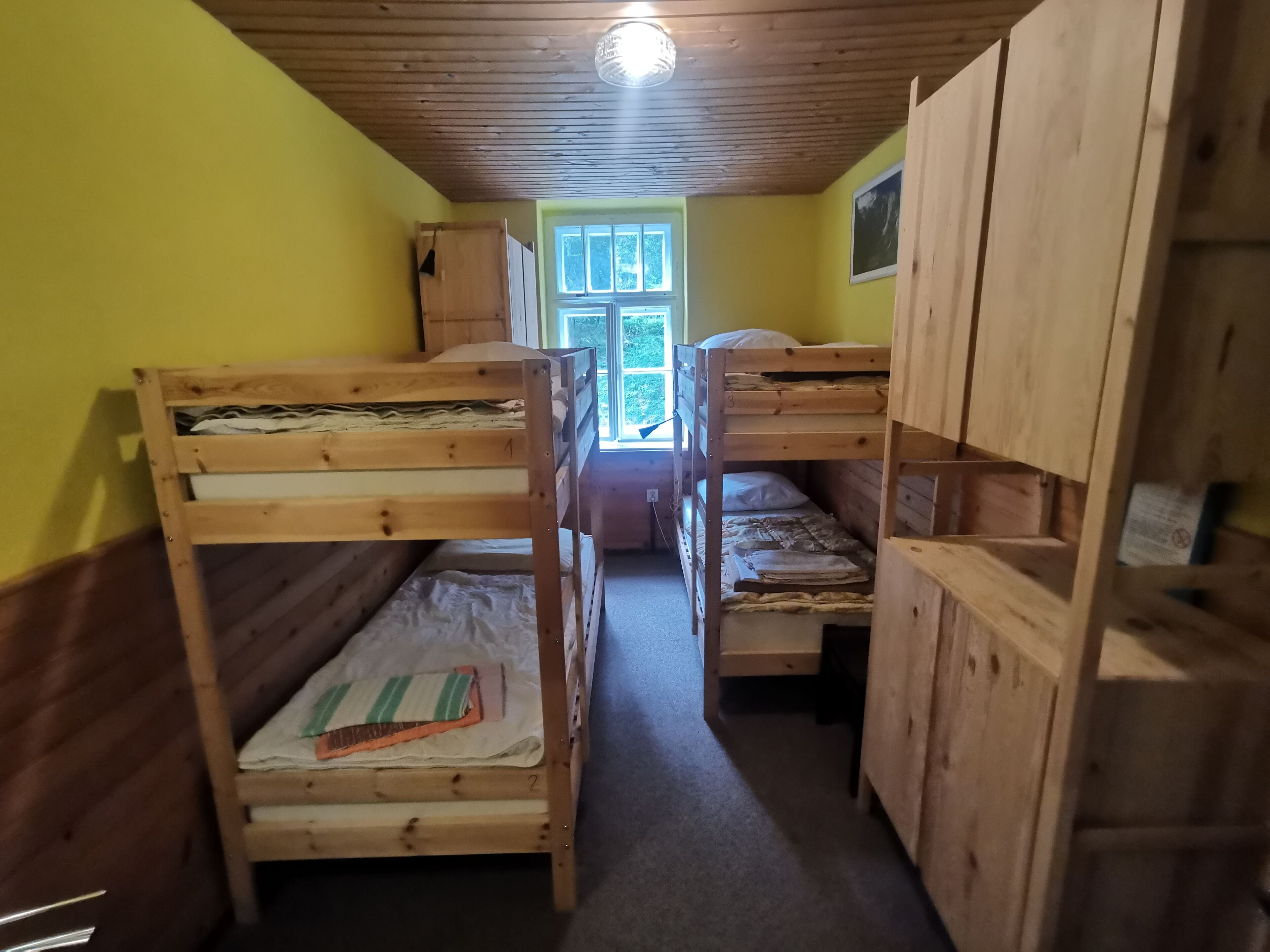 Une pièce avec des lits superposés, des murs en bois, une fenêtre et un luminaire au plafond.