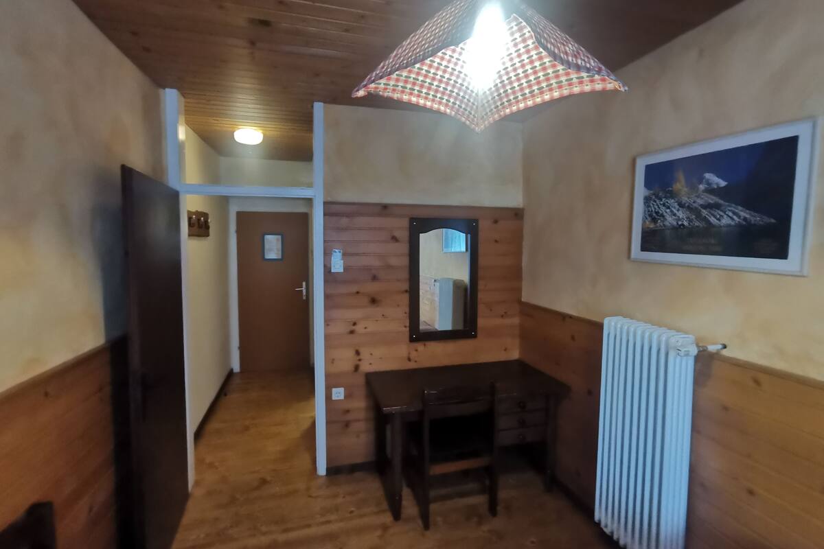 A wooden-paneled room with a table and chair, a radiator, a mirror, and a framed picture on the wall.