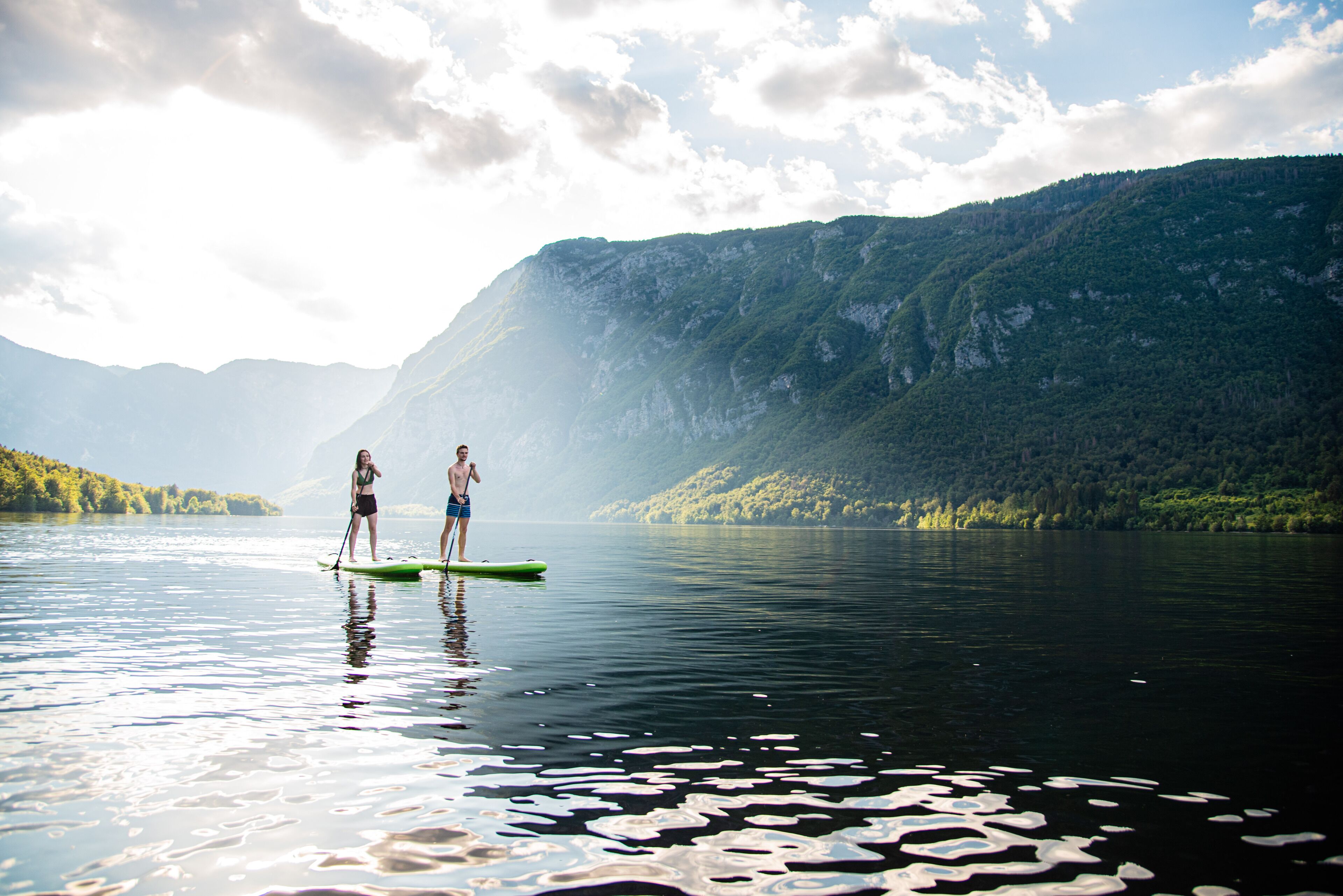 Two people paddleboarding on a calm lake with mountains in the background.