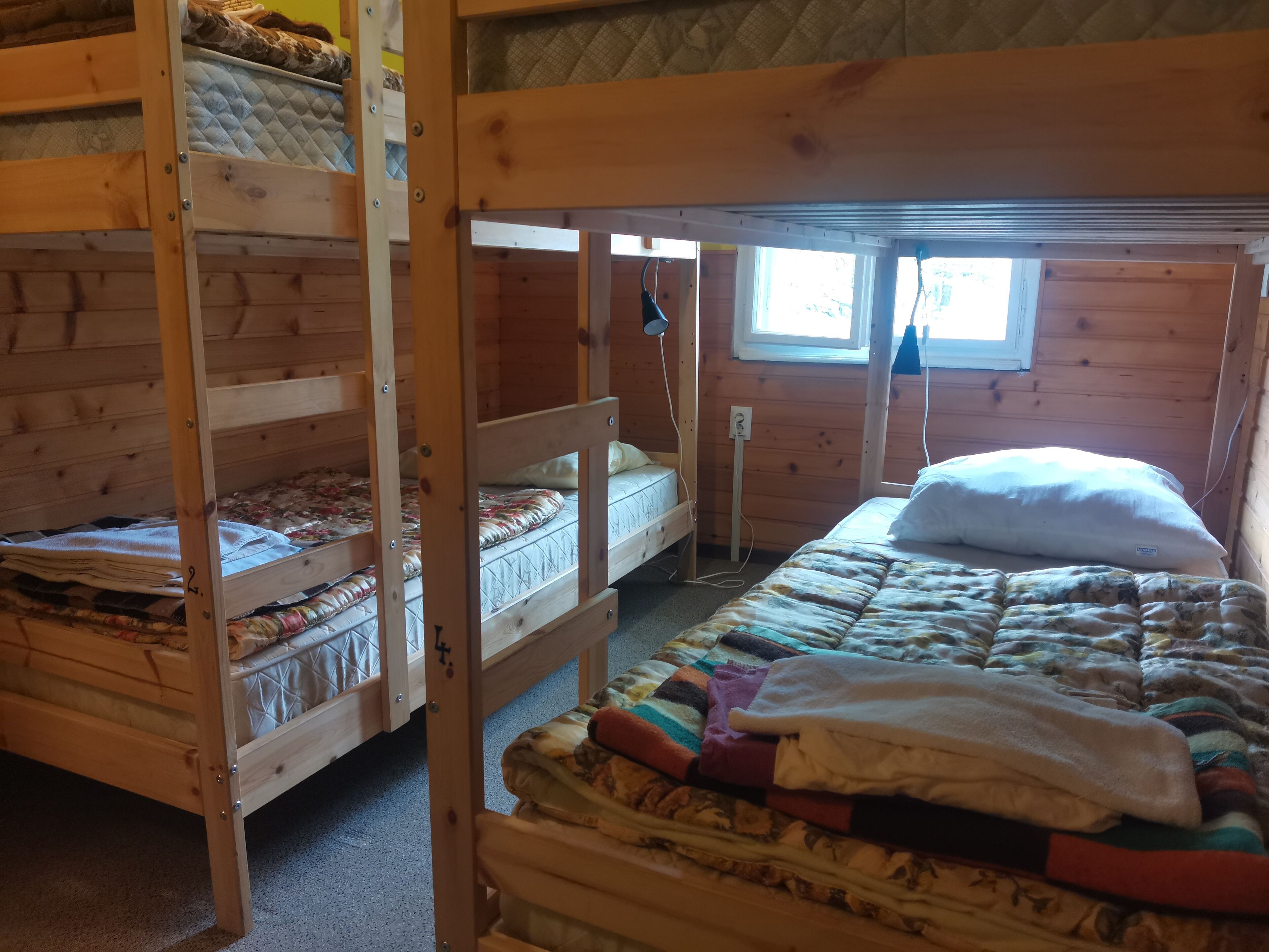 A bunk bed room with a window, wooden walls, and a quilted bedspread.