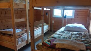 A bunk bed room with a window, wooden walls, and a quilted bedspread.