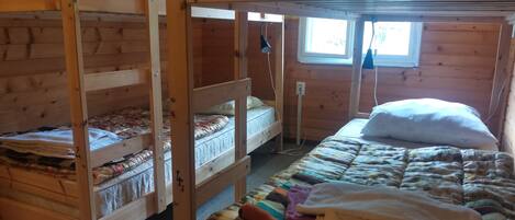 Dormitorio con literas, ventana, paredes de madera y colcha acolchada.