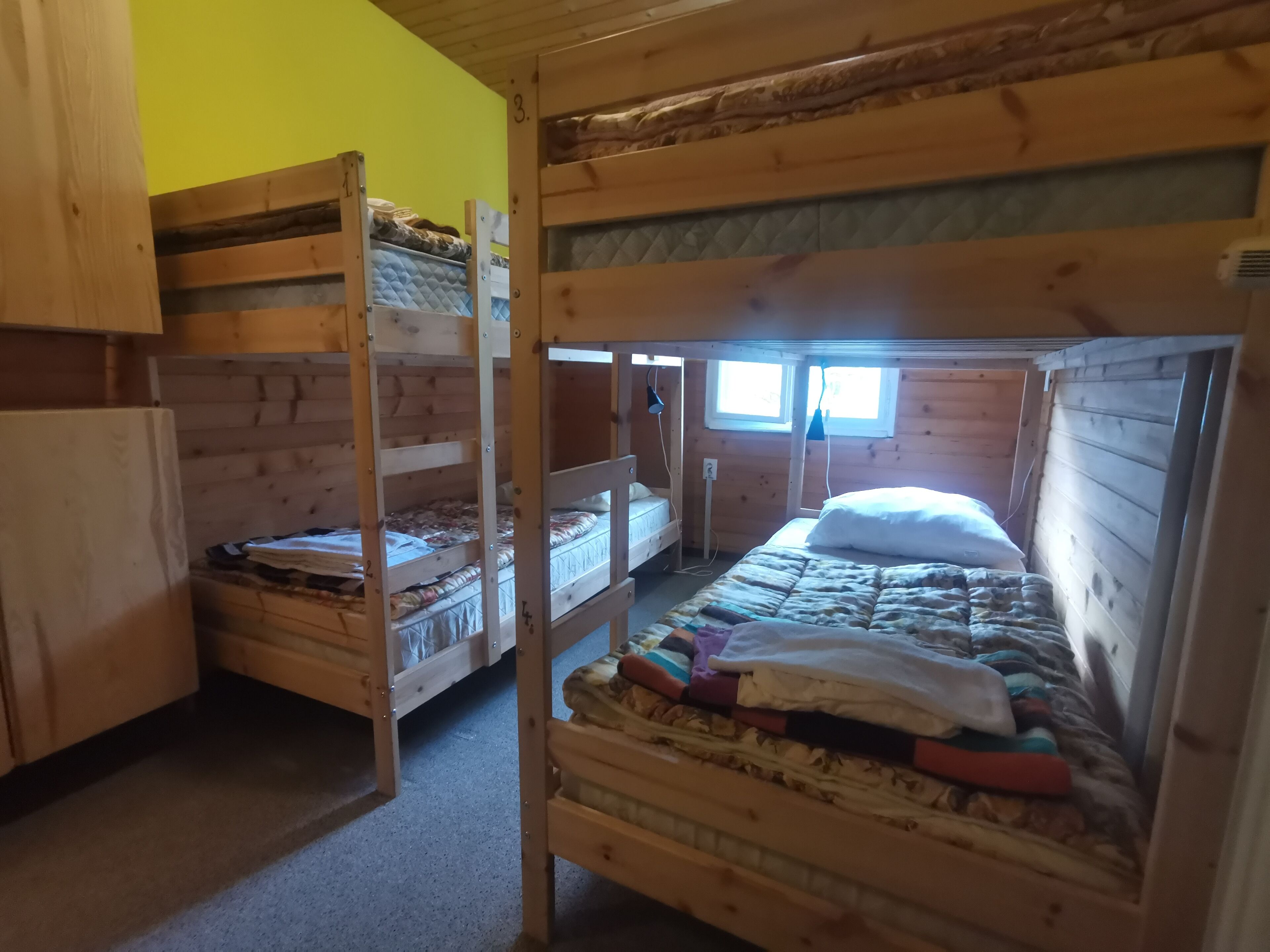 A dormitory room with bunk beds, wooden walls, and a window providing natural light.