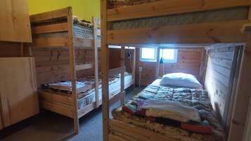 A dormitory room with bunk beds, wooden walls, and a window providing natural light.