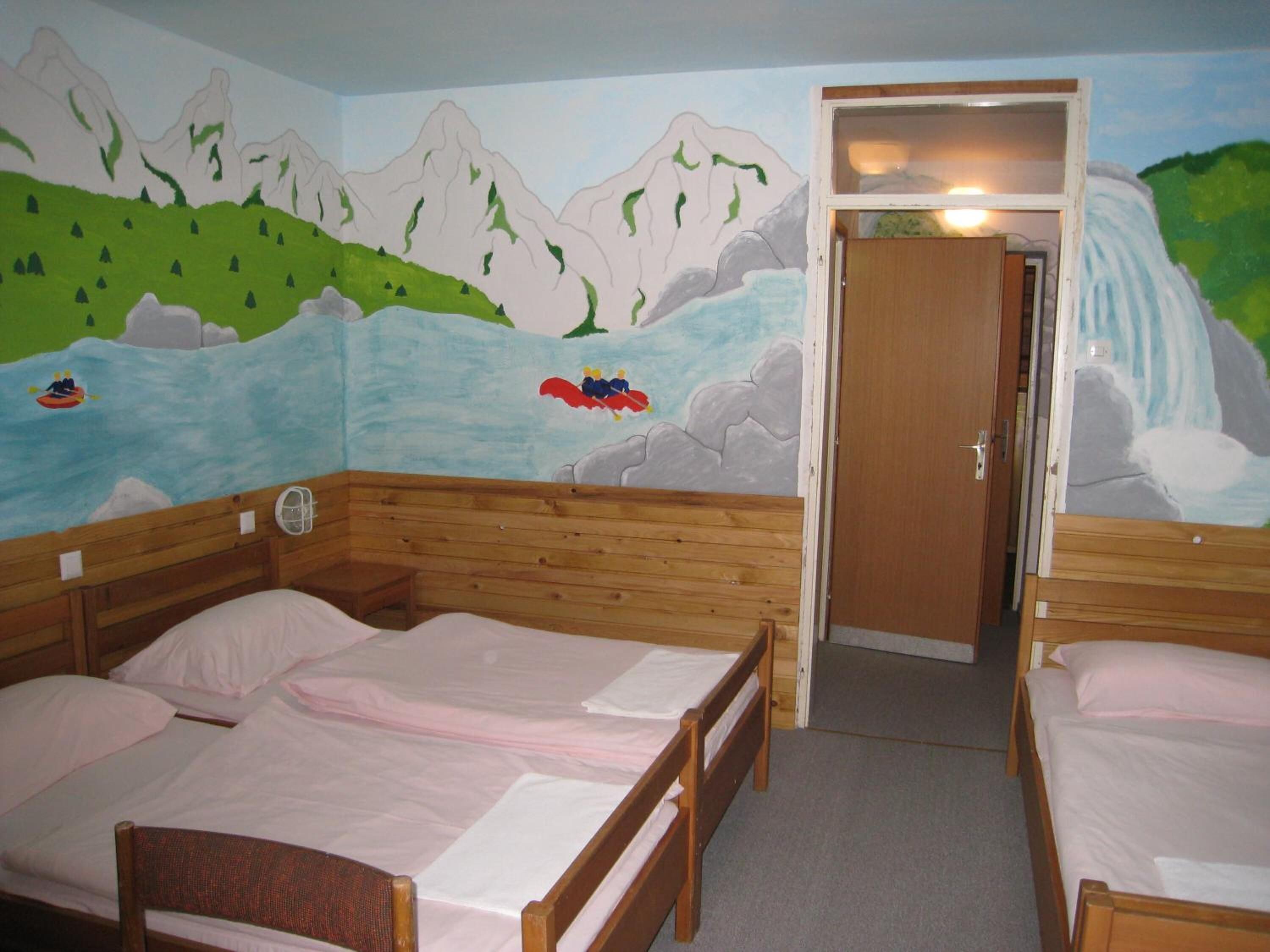 A room with two wooden beds, a mural of a mountainous landscape, and a door leading to another room.