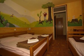 A room with three wooden beds, each with a mattress and a blanket. There is a mural on the wall depicting a forest scene with a person and a deer. - Hostel pod Voglom (Bohinj)