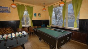 A pool table in a room with a foosball table, wooden flooring, and green curtains.