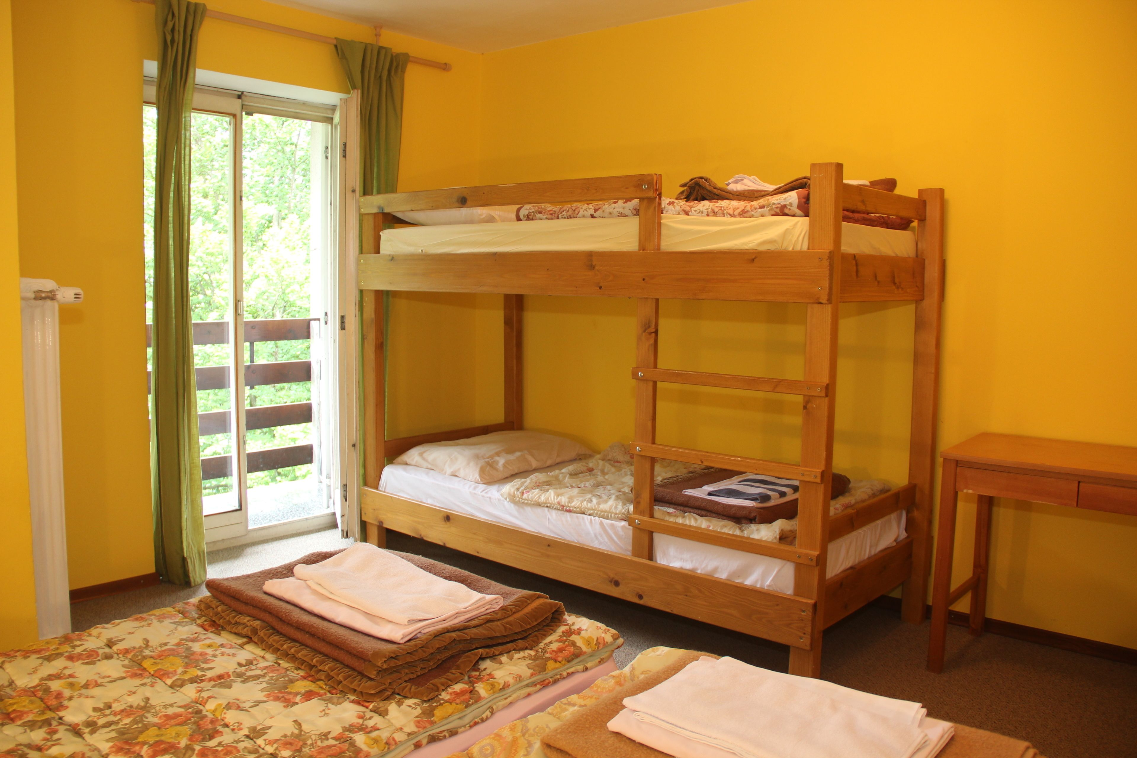 Een slaapkamer met een stapelbed met houten frame, een tafeltje en een raam met gordijnen.